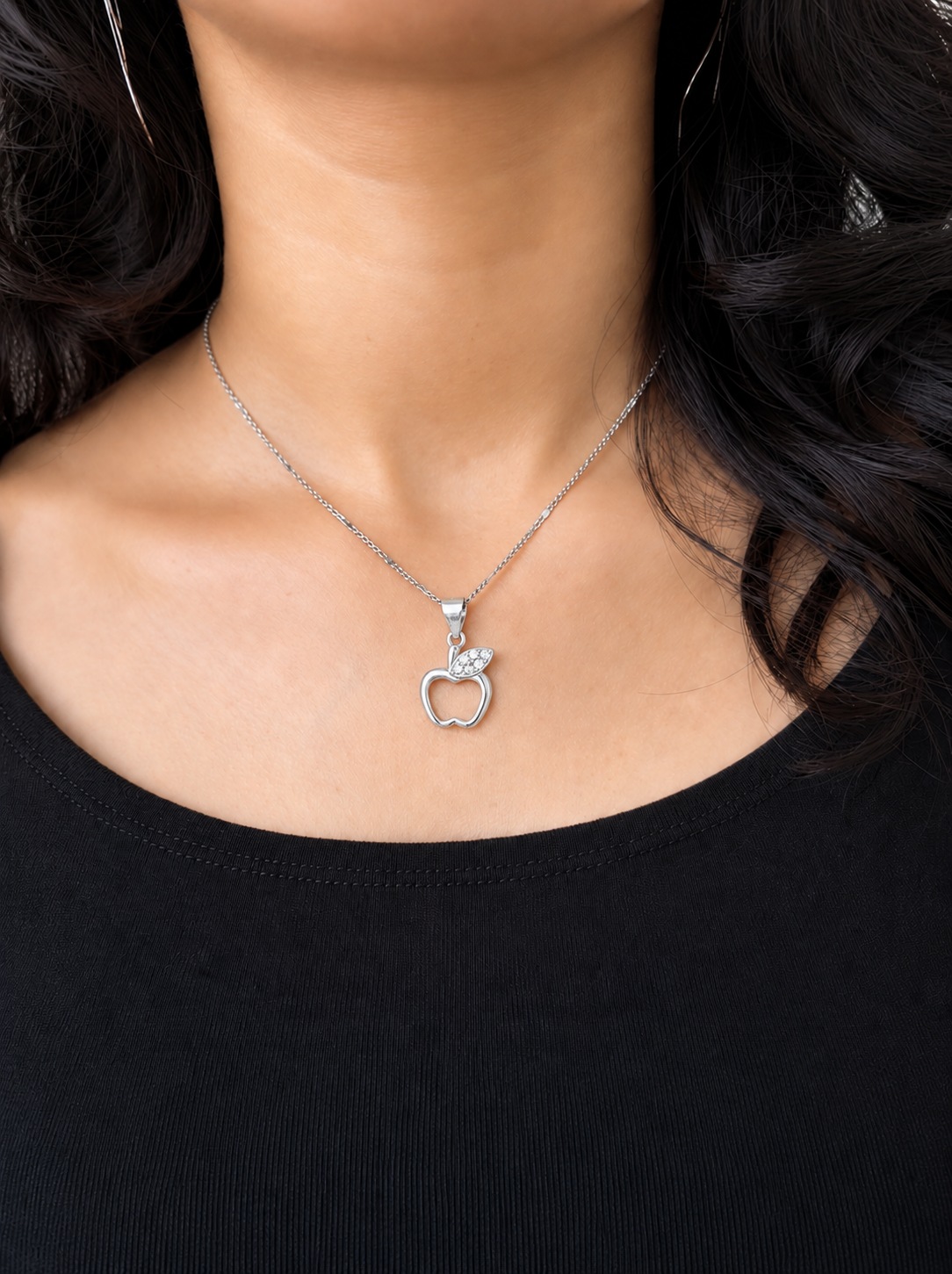 A close-up of a model wearing a silver chain necklace with a small apple-shaped pendant, paired with a black top.
