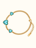 Gold chain bracelet with three heart-shaped turquoise blue crystals, displayed on a clean off-white background.