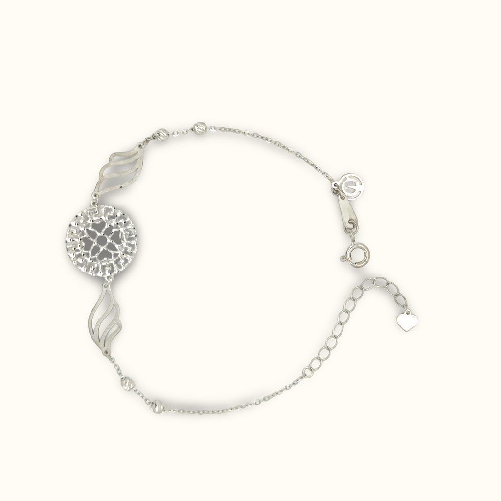 A silver-toned delicate chain bracelet featuring a textured circular medallion, two stylized leaf charms, and a small heart charm, displayed on a clean off-white background.