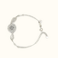 A silver-toned delicate chain bracelet featuring a textured circular medallion, two stylized leaf charms, and a small heart charm, displayed on a clean off-white background.