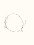 A delicate silver chain bracelet featuring three textured heart charms and a small heart-shaped tag, displayed on a solid off-white background.