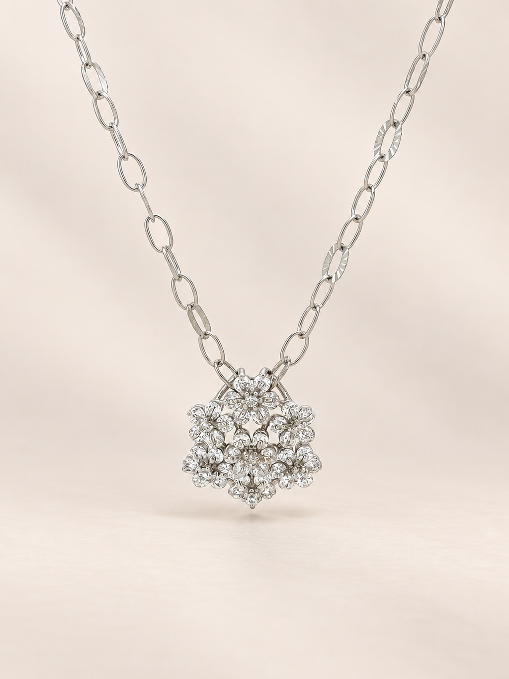 A silver-tone necklace with a pavé diamond pendant, displayed against a soft beige background.