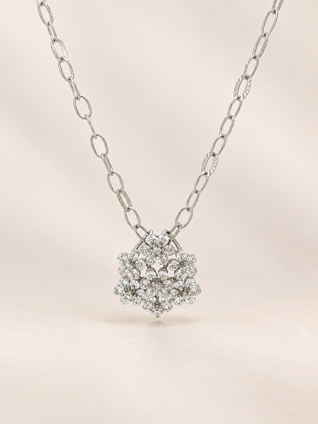 A silver-tone necklace with a pavé diamond pendant, displayed against a soft beige background.