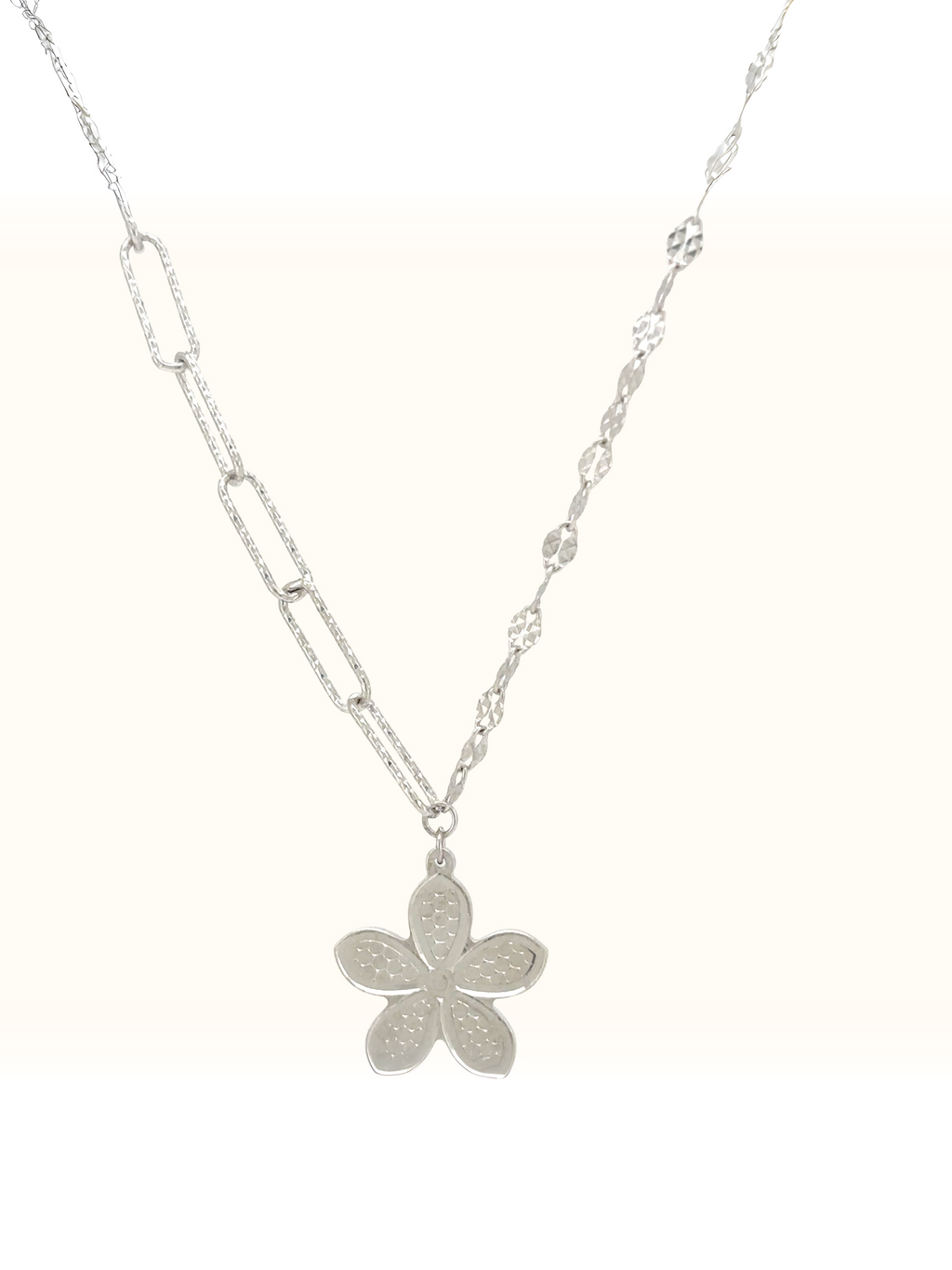 A silver-toned layered necklace featuring a textured five-petal flower pendant, displayed against a clean off-white background.