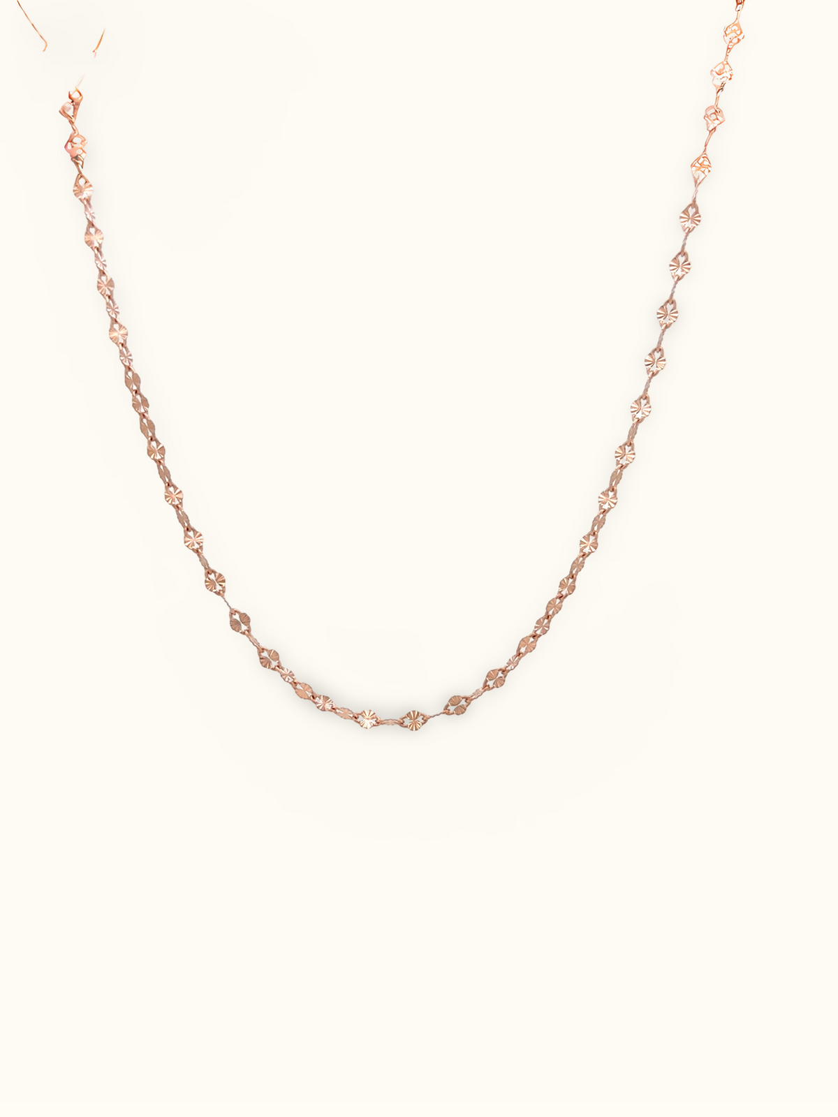 A delicate rose gold chain necklace with small twisted links, displayed against a solid off-white background.