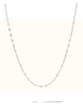 A delicate silver-toned tennis necklace featuring small, clear round-cut gemstones set along a fine chain, displayed against a solid off-white background.