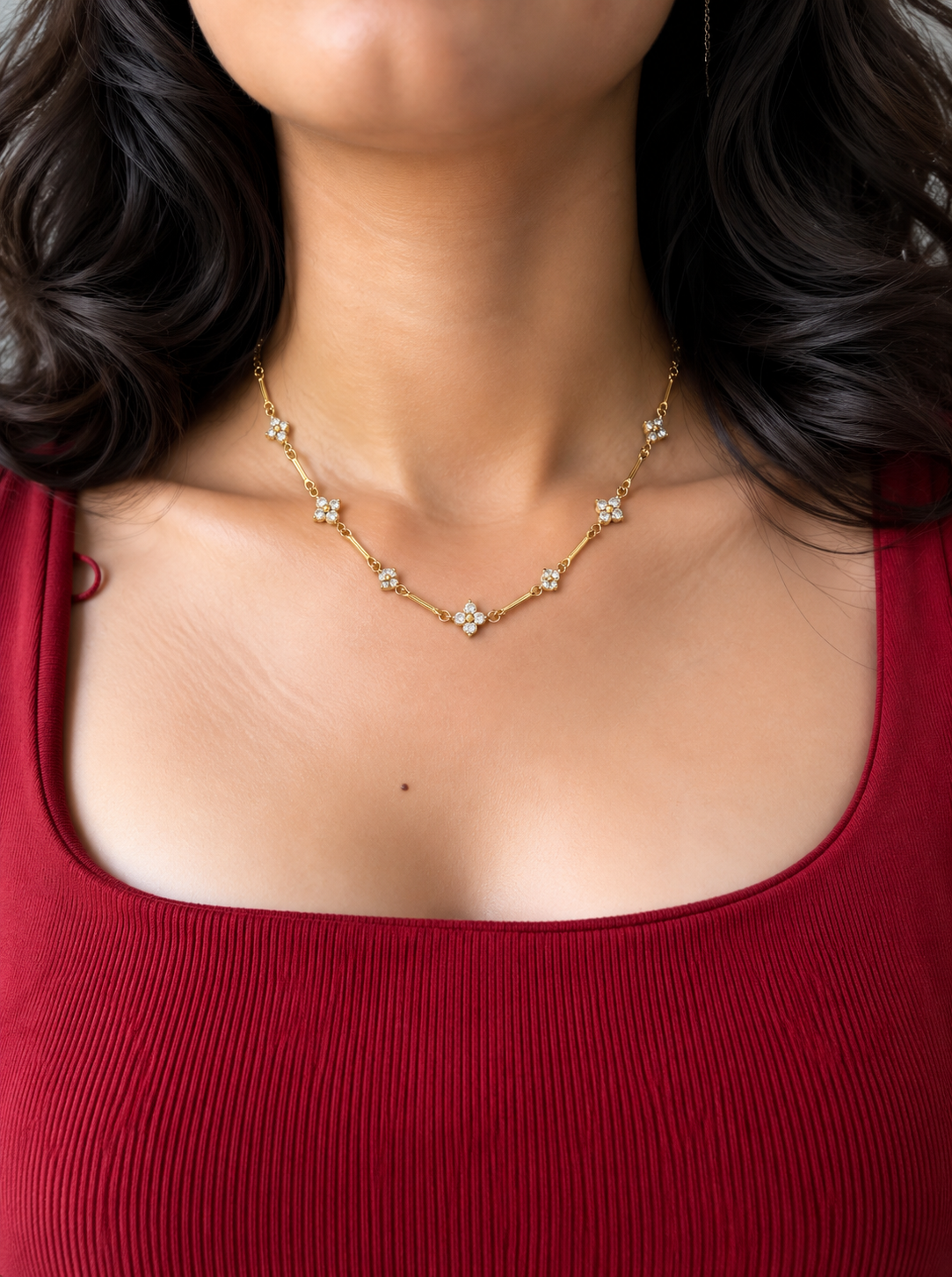 Gold-toned floral link necklace featuring four-petal flower motifs with clear sparkling stones and polished gold centres.

Close-up of a delicate gold-tone necklace with floral accents connected by elongated links worn by a model.