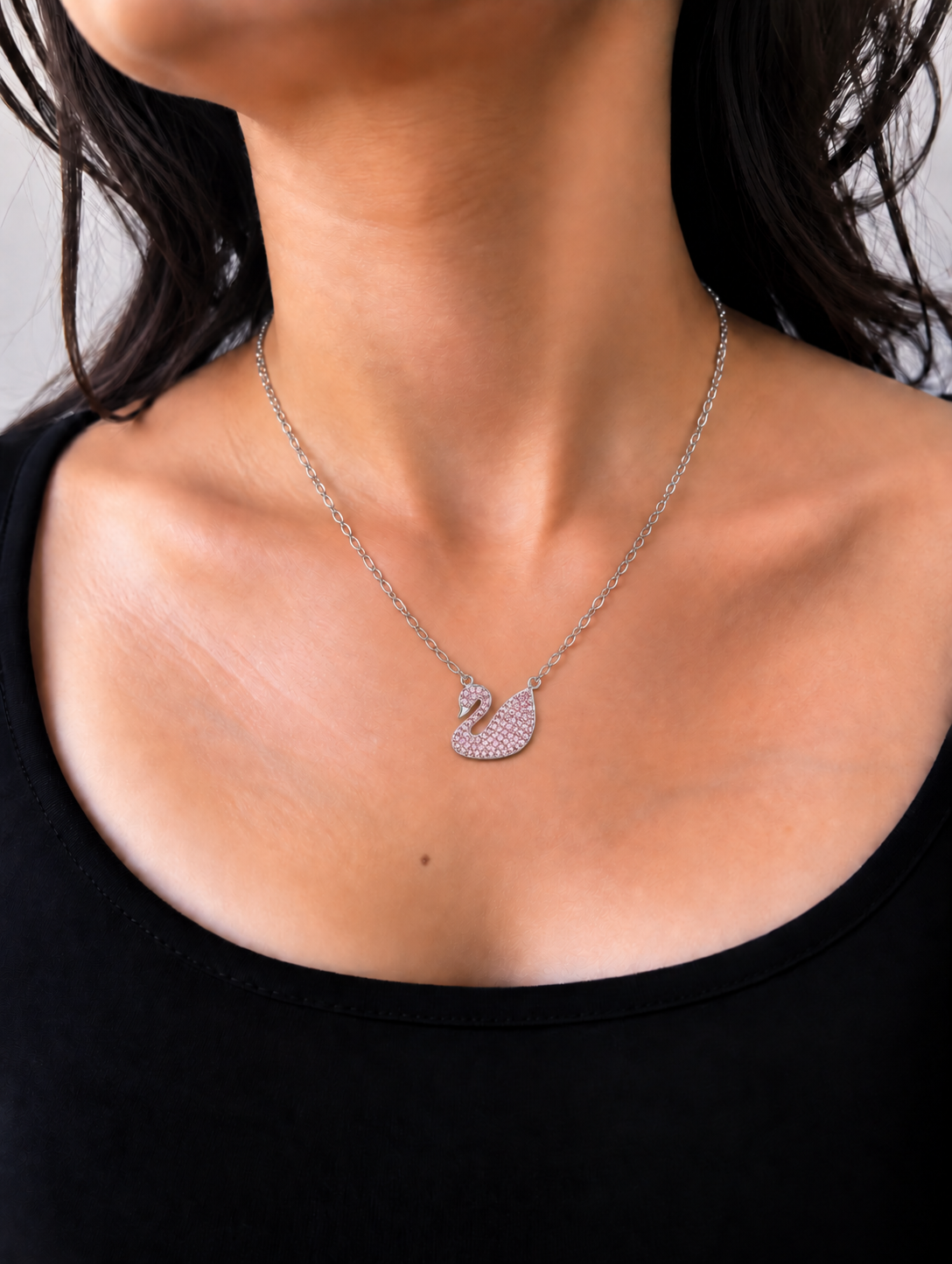 Silver-toned swan pendant necklace embellished with blush-pink sparkling stones and polished detailing.
Elegant pink swan charm suspended from a delicate silver-toned link chain worn by a model.