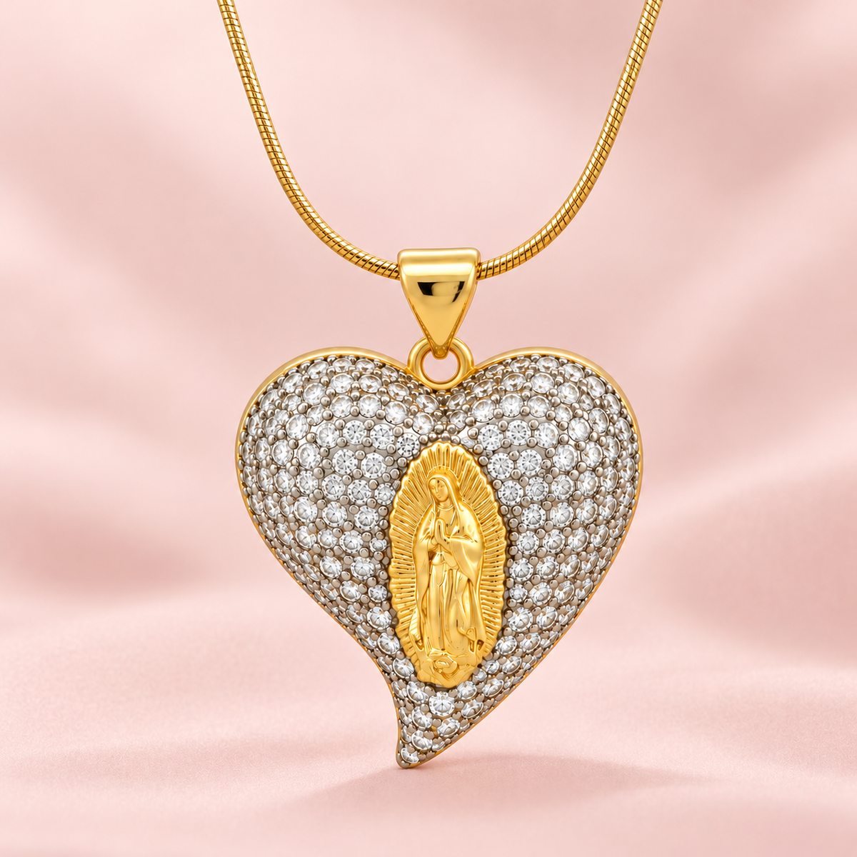 Gold-toned snake chain necklace with a heart-shaped pendant covered in clear sparkling stones and a raised golden religious figure at the centre.

Statement heart pendant necklace featuring silver-toned pavé detailing and gold accents, displayed against a pink background.