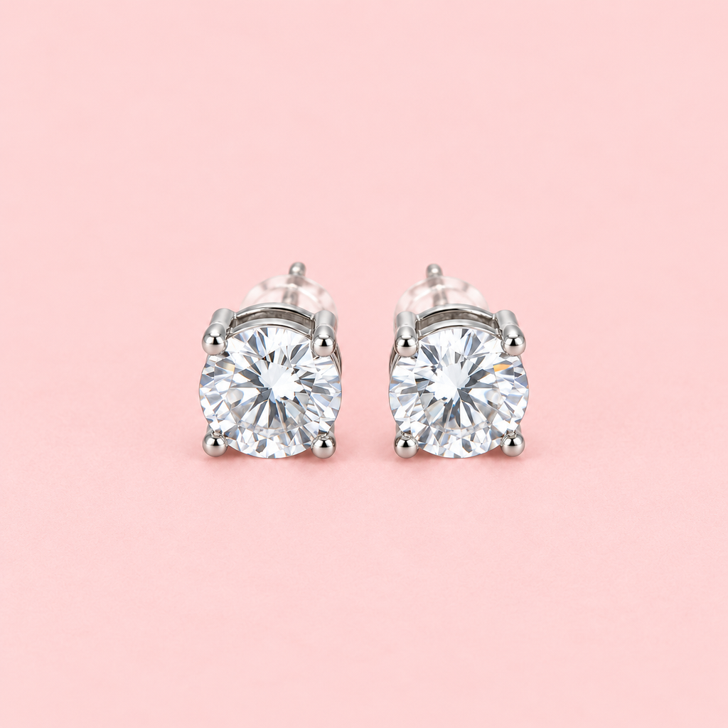 Silver-tone round solitaire stud earrings with large clear stones in four-prong settings displayed against a pink background.