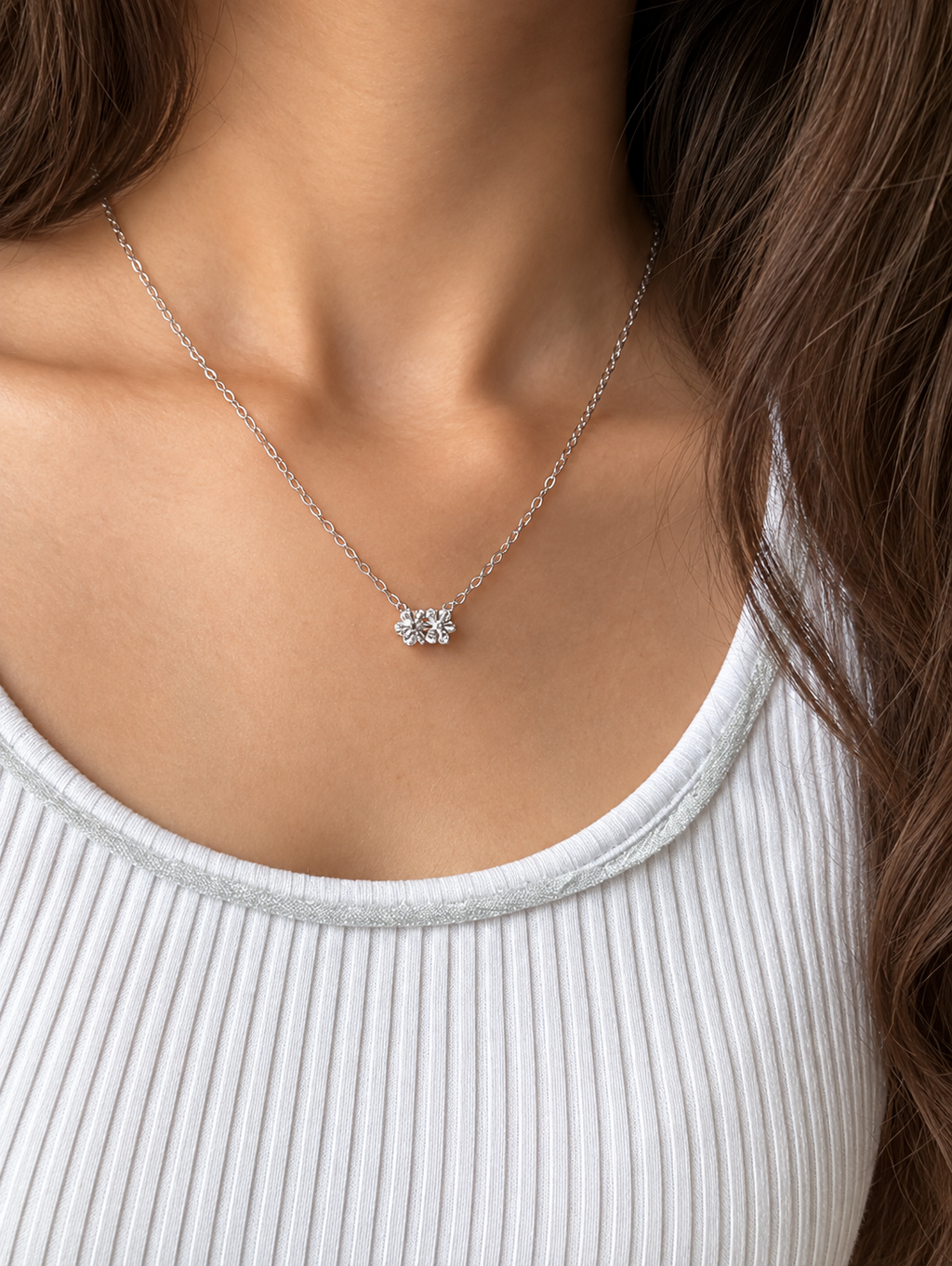 A silver-toned chain necklace featuring a small cluster of clear gemstones in a flower setting, displayed against a model wearing a white top.