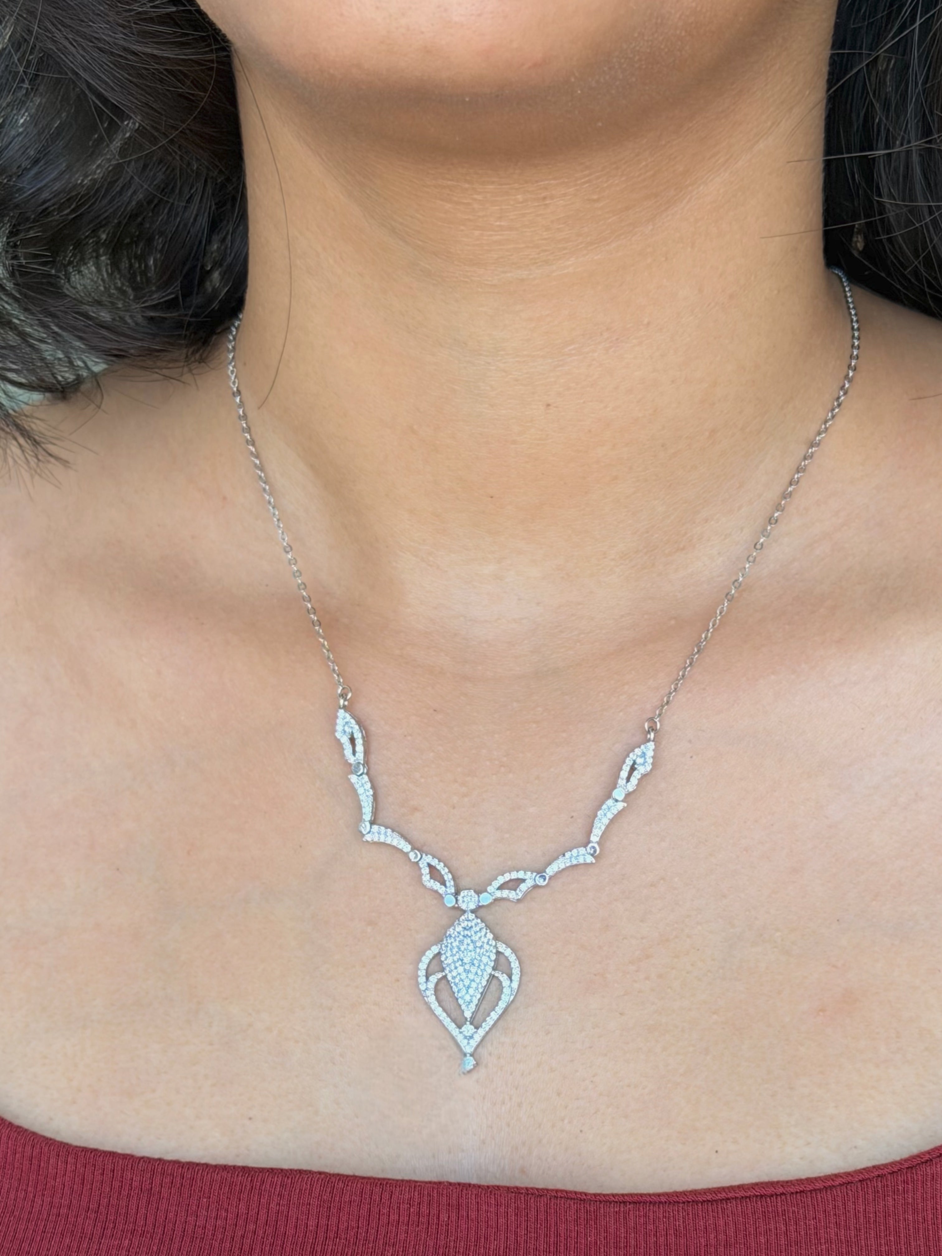 A close-up of a model's neck wearing a delicate silver necklace with a teardrop-shaped pendant adorned with small clear stones.