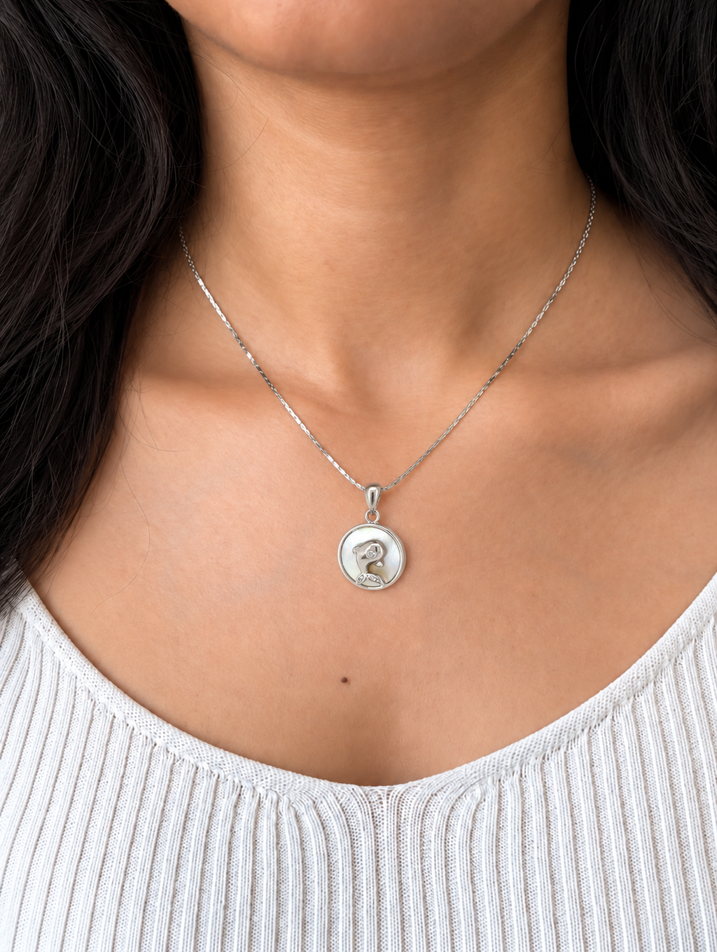 A silver pendant necklace featuring a circular charm with a polished silver dog silhouette and a small clear gemstone, suspended from a delicate silver chain which is worn by a model wearing a white top.