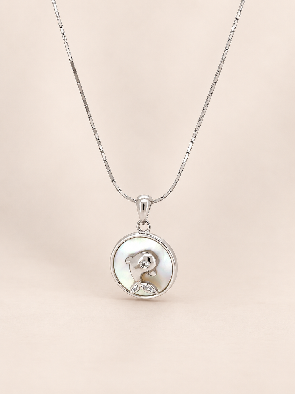 A silver pendant necklace featuring a circular charm with a polished silver dog silhouette and a small clear gemstone, suspended from a delicate silver chain against a soft beige background.