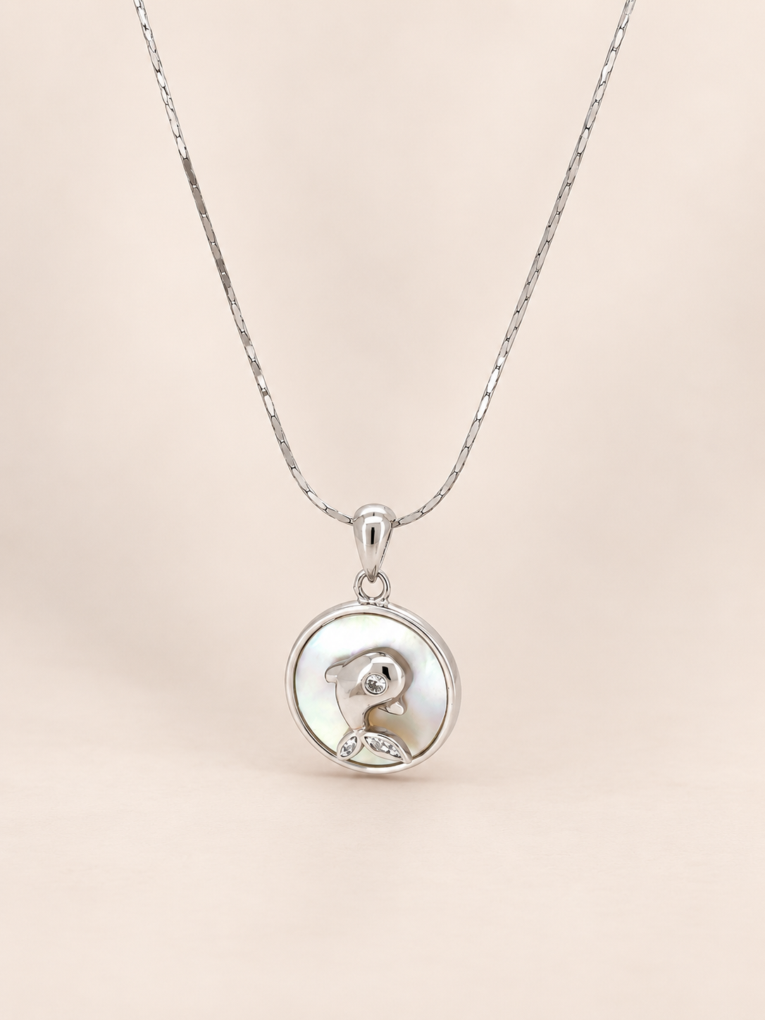 A silver pendant necklace featuring a circular charm with a polished silver dog silhouette and a small clear gemstone, suspended from a delicate silver chain against a soft beige background.
