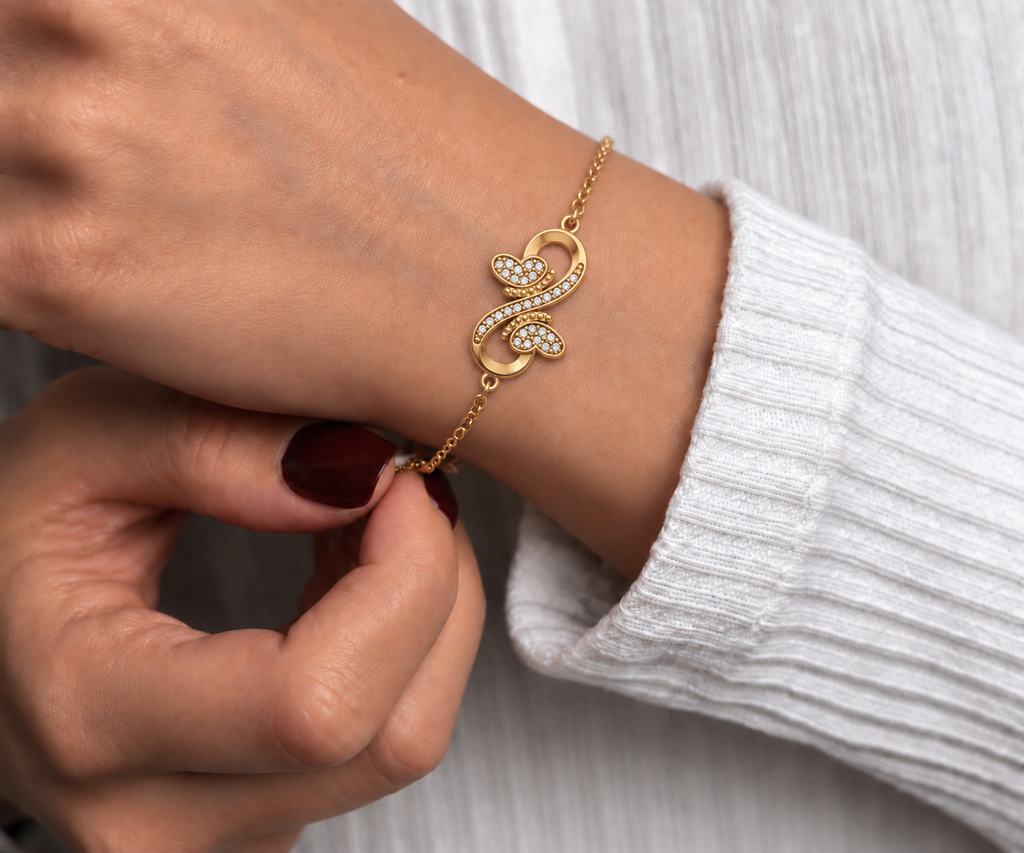 A delicate gold chain bracelet with a infinity design and two hearts facing each other filled with diamonds worn by a model.