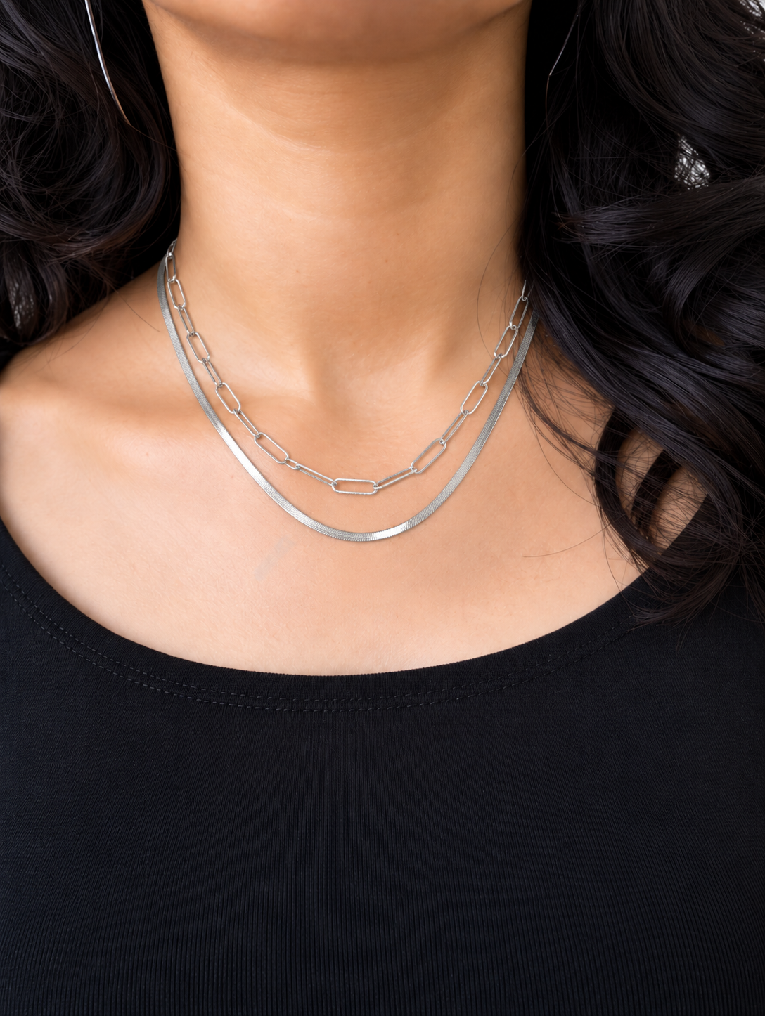 A silver-toned double-strand necklace featuring a thick textured outer chain and a thinner inner chain with elongated rectangular links, displayed against a model wearing a black top.