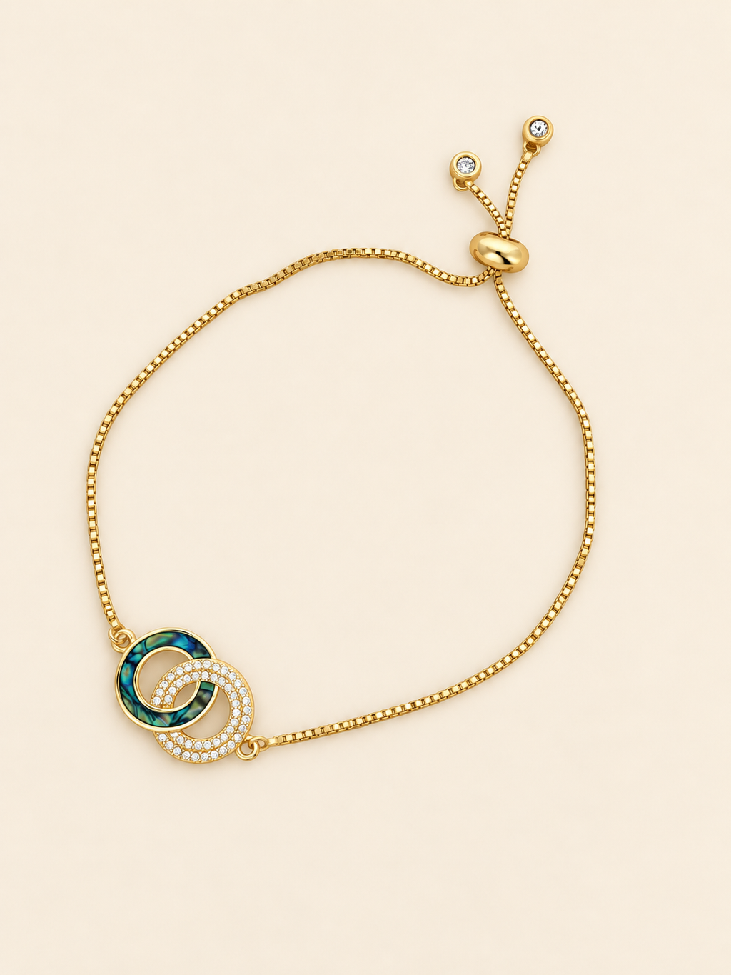 Gold-toned stainless steel bracelet featuring two intertwined circles, one with green enamel and the other set with sparkling white stones.
Delicate chain bracelet with an adjustable slider closure, displayed on a clean pink background.