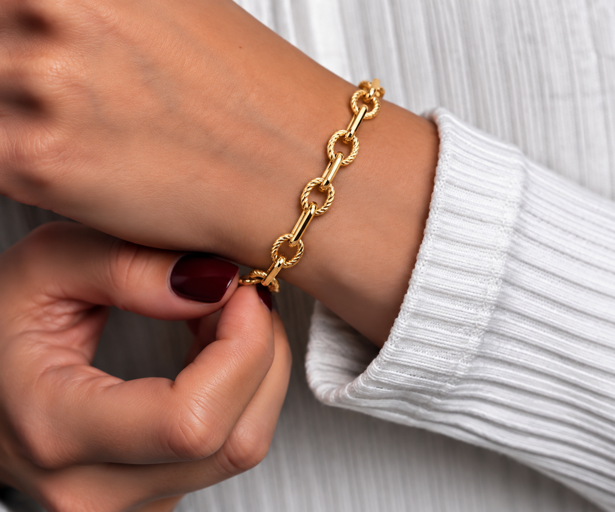 Gold-toned stainless steel chain bracelet featuring twisted rope-style links connected by elongated polished bar links.
Statement link bracelet with a shiny golden finish and lobster clasp, worn by a model.