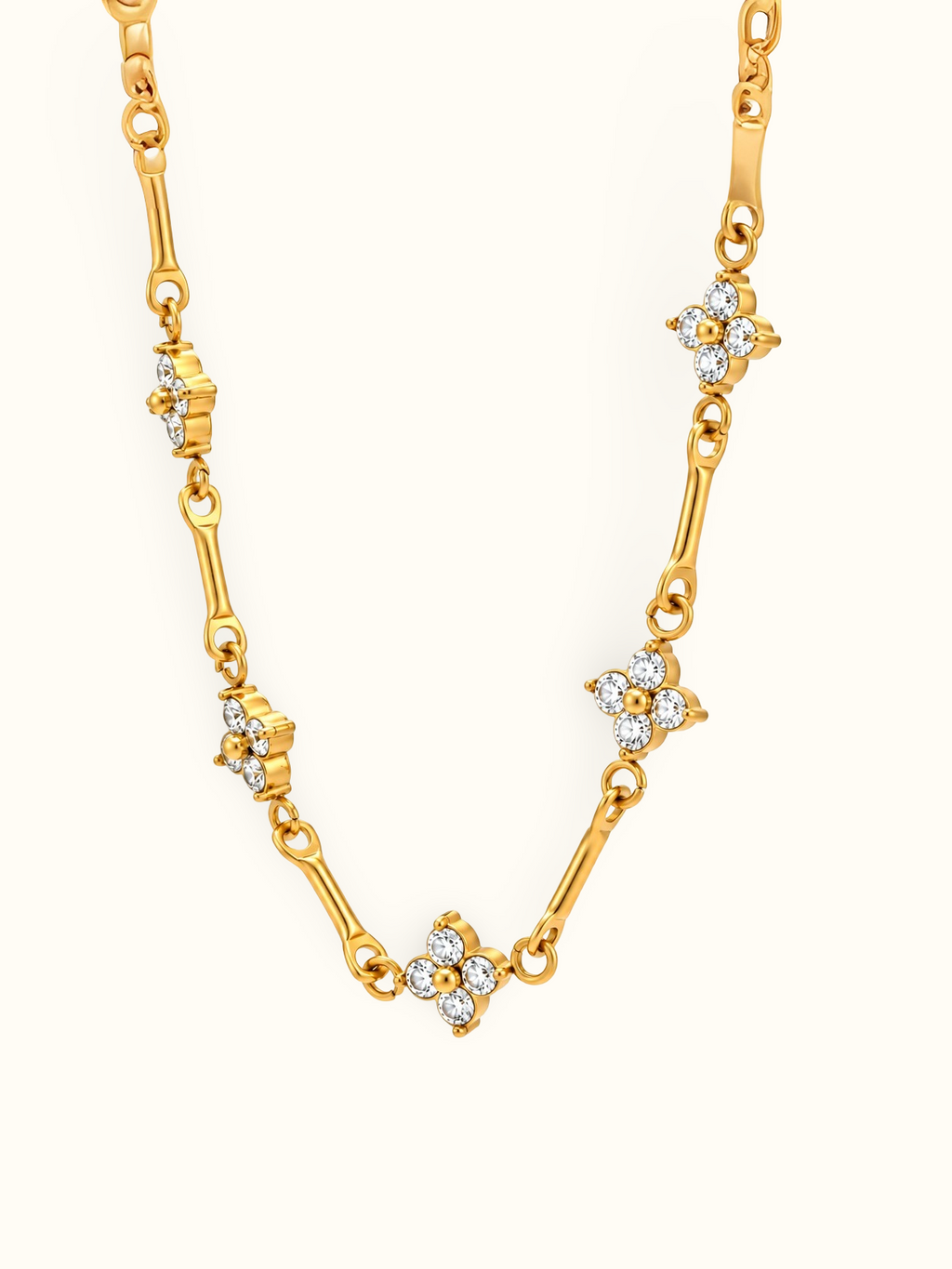Gold-toned floral link necklace featuring four-petal flower motifs with clear sparkling stones and polished gold centres.

Close-up of a delicate gold-tone necklace with floral accents connected by elongated links against a white background.