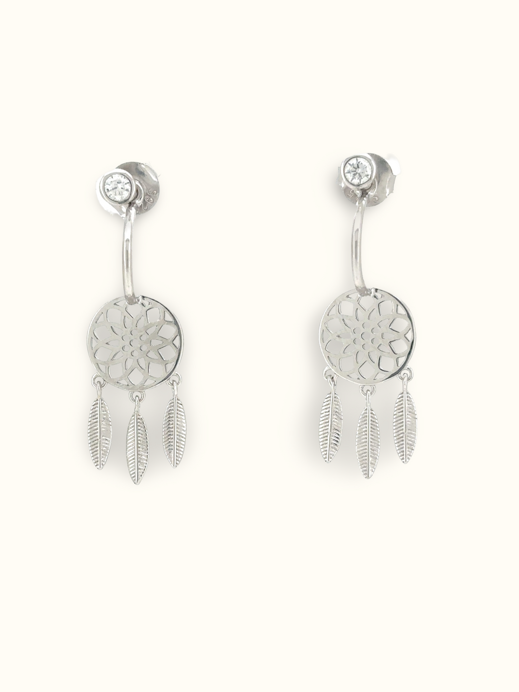 A pair of silver dreamcatcher dangle earrings with a circular filigree center, a small clear rhinestone stud above, and three dangling feather charms, shown on a plain off-white background.