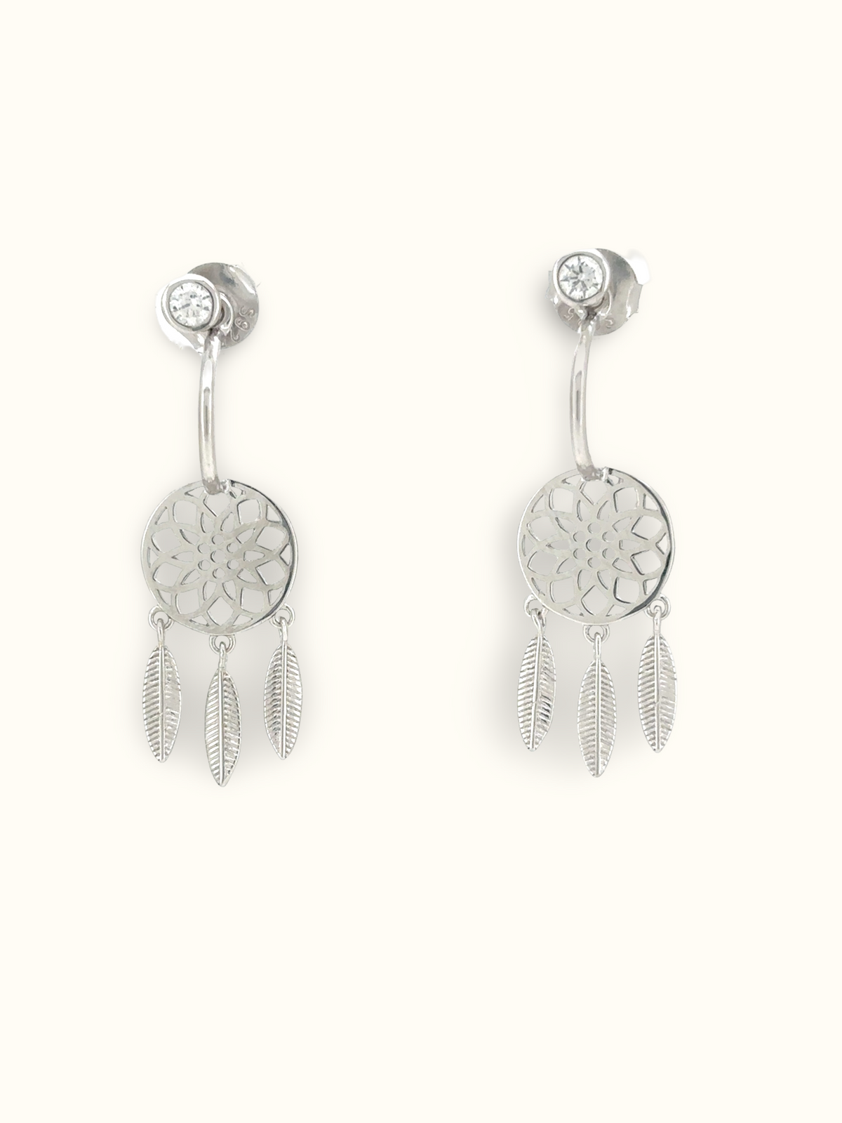 A pair of silver dreamcatcher dangle earrings with a circular filigree center, a small clear rhinestone stud above, and three dangling feather charms, shown on a plain off-white background.