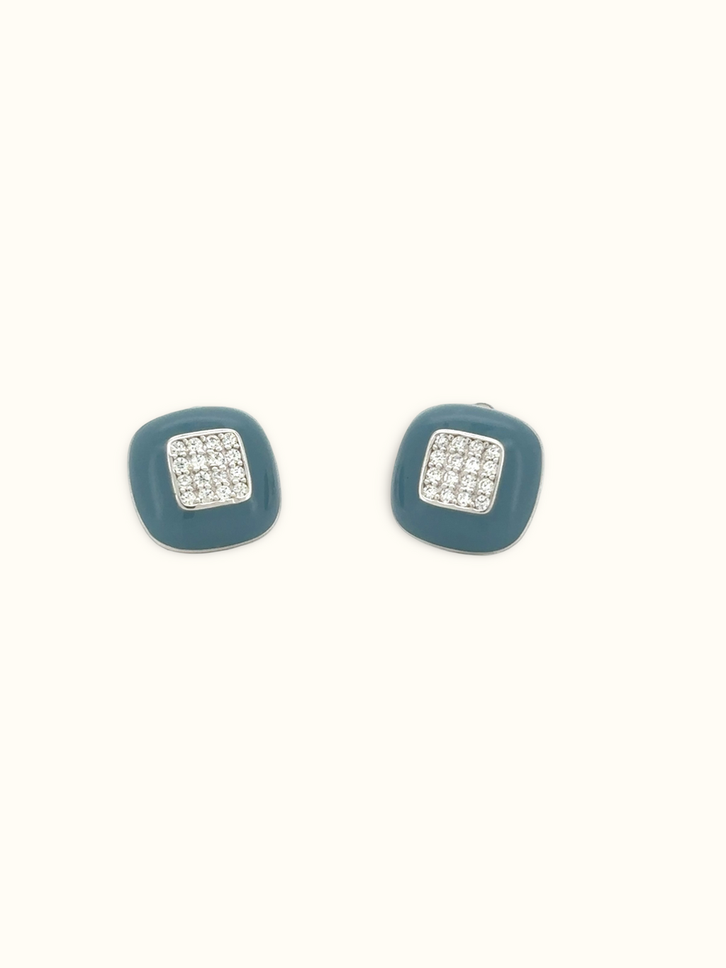 A pair of square stud earrings with a muted teal-blue enamel body and a central silver-toned square set with clear pavé stones, shown on a plain off-white background.