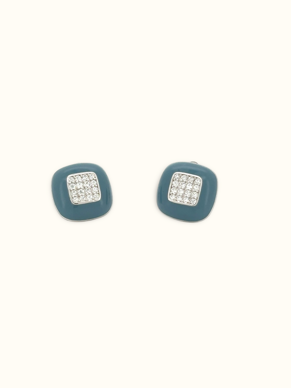 A pair of square stud earrings with a muted teal-blue enamel body and a central silver-toned square set with clear pavé stones, shown on a plain off-white background.