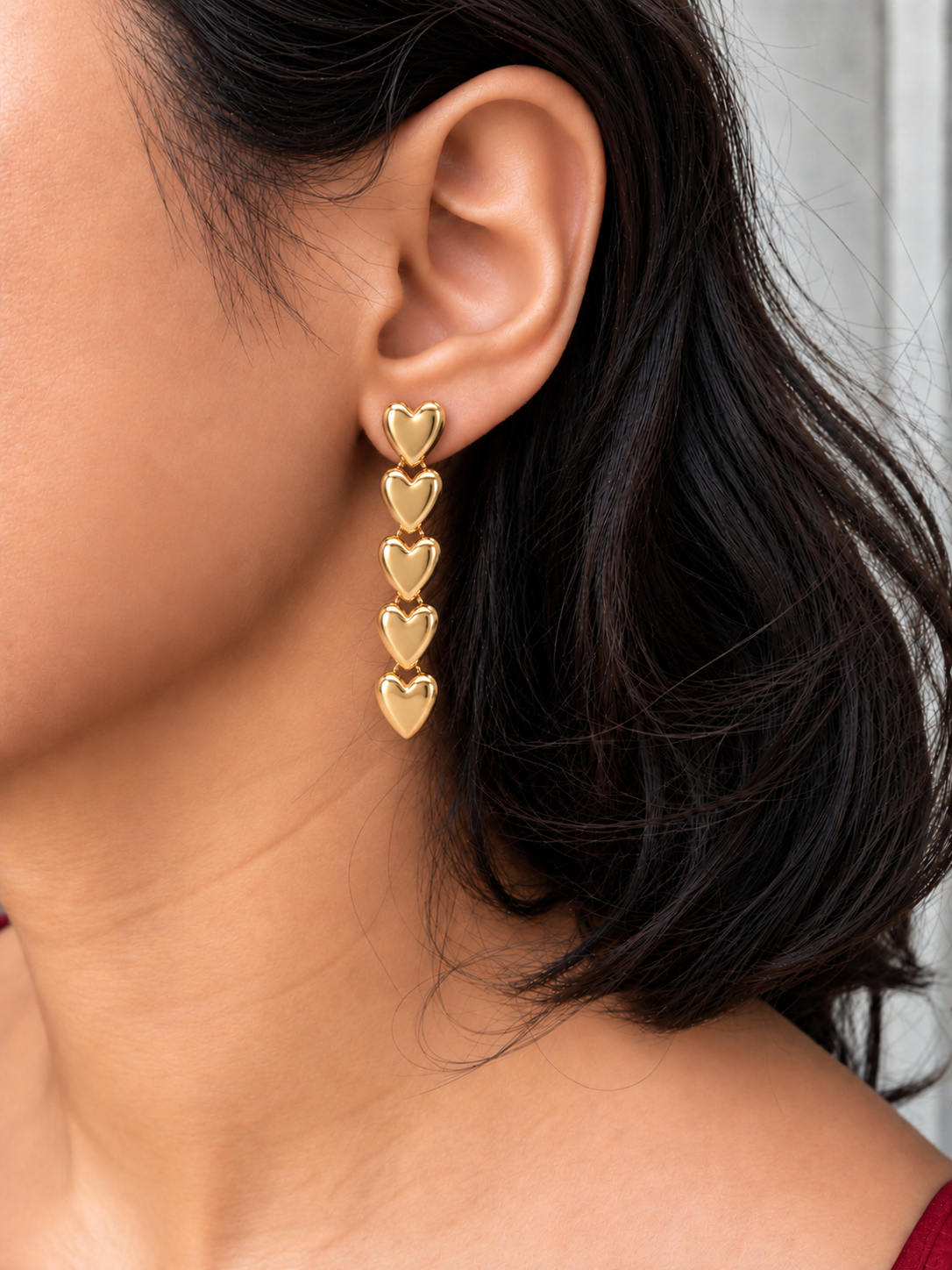 Gold-tone drop earrings featuring five connected polished heart charms in a vertical design worn by a model.