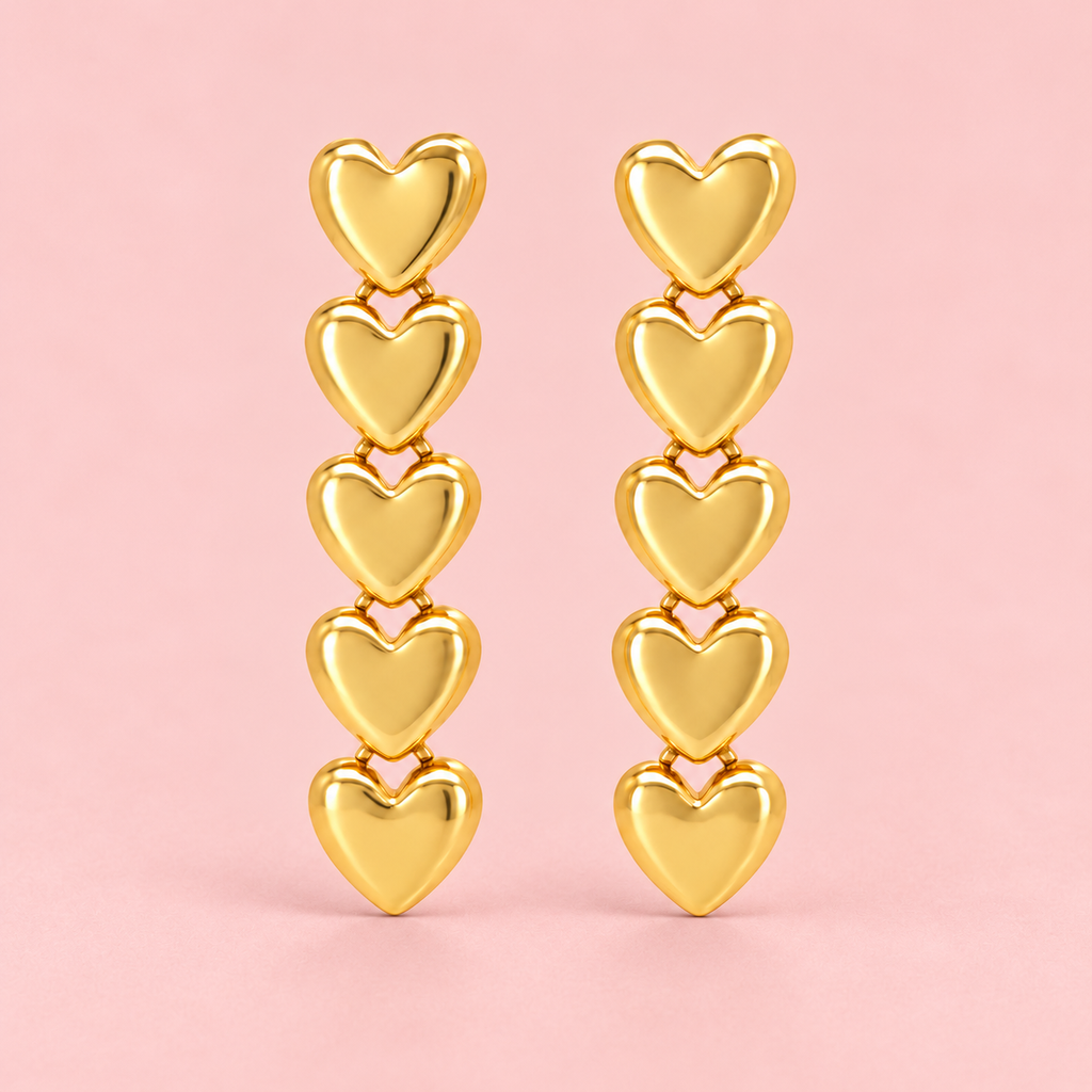 Gold-tone drop earrings featuring five connected polished heart charms in a vertical design displayed against a pink background.