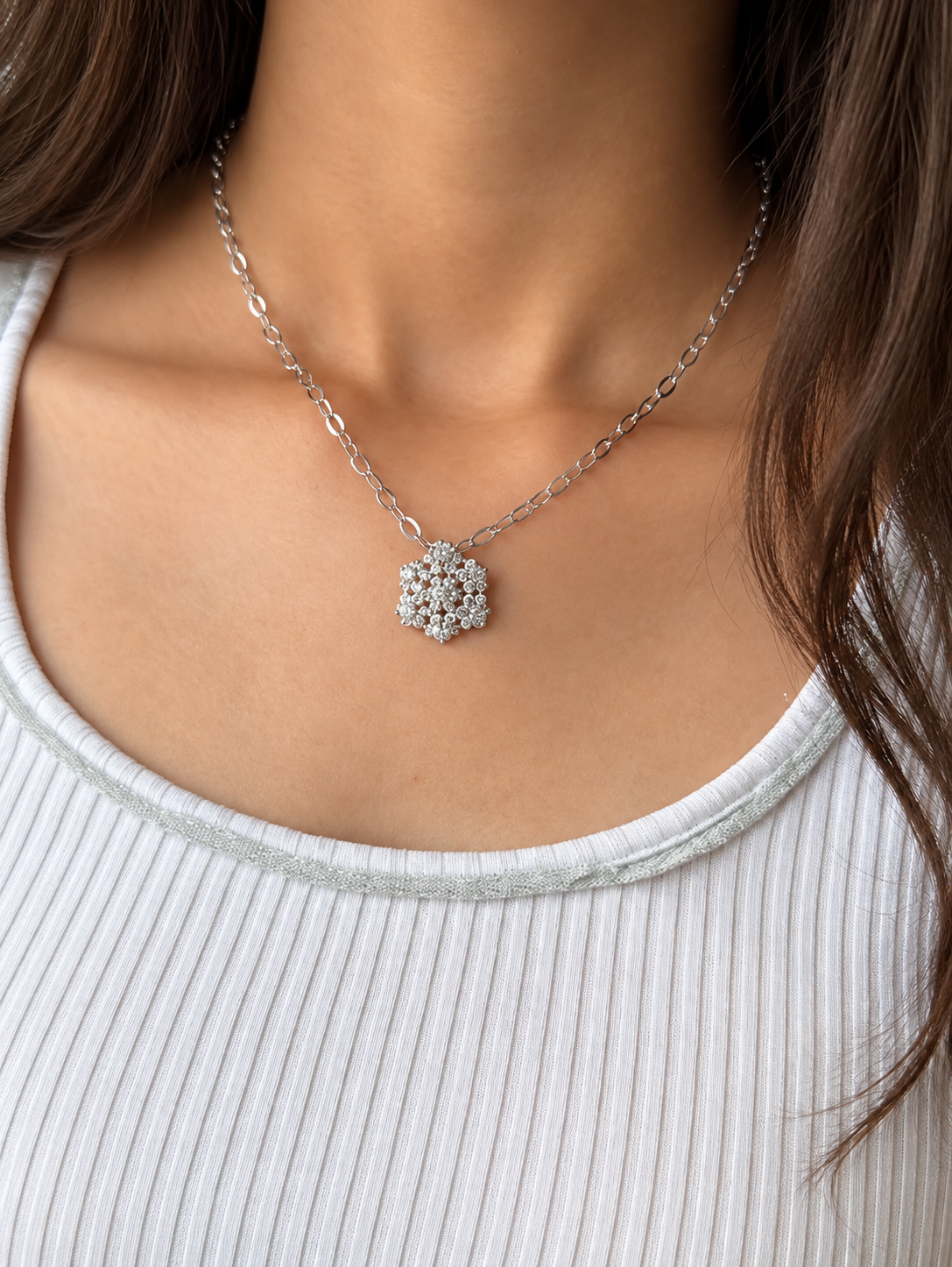 A silver-toned necklace featuring a delicate paperclip chain and a central cluster pendant set with clear gemstones, worn by a model.