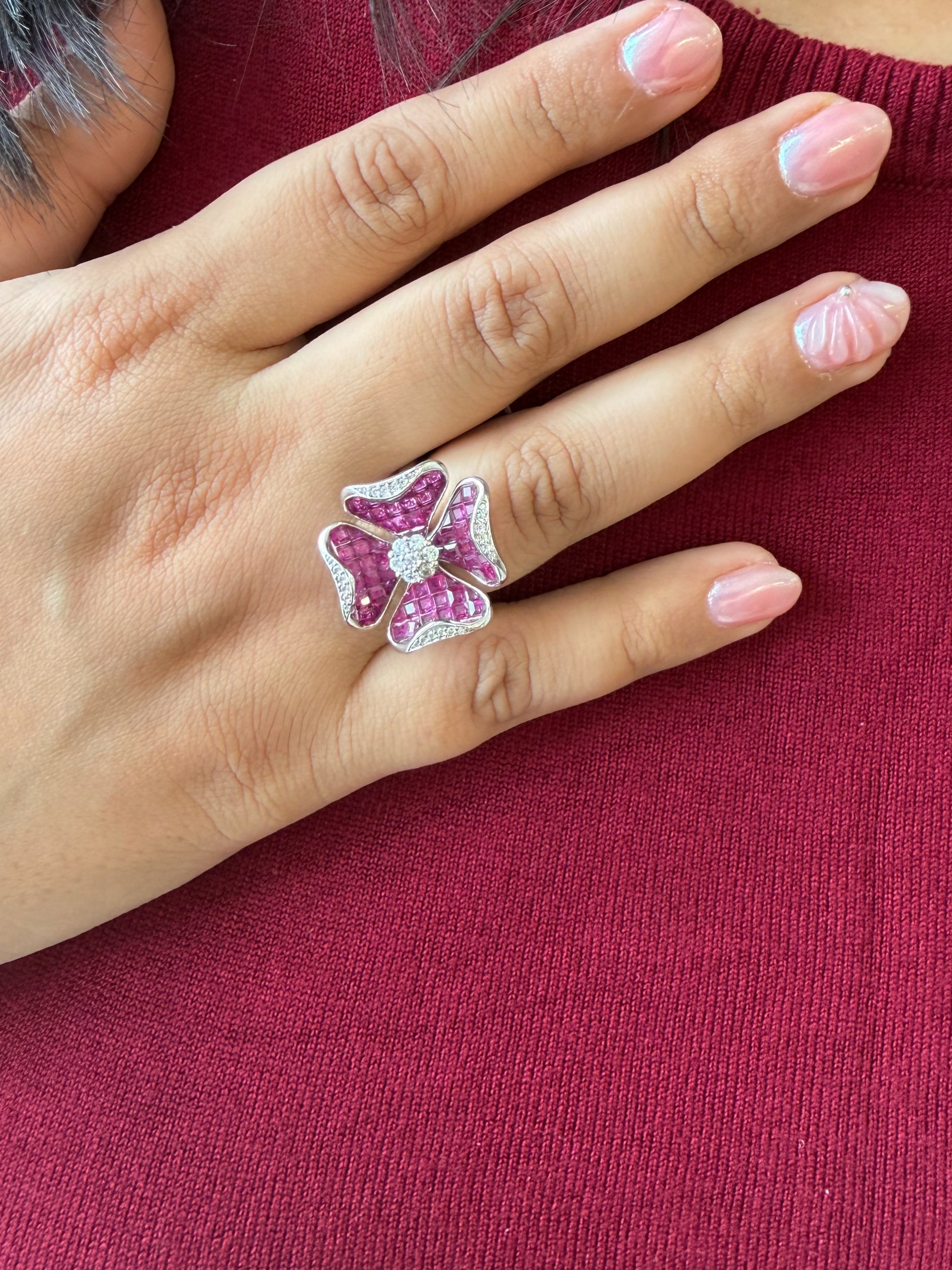 A close-up of a hand wearing a silver-toned flower ring set with pink gemstones, resting against a dark pink knit sweater.