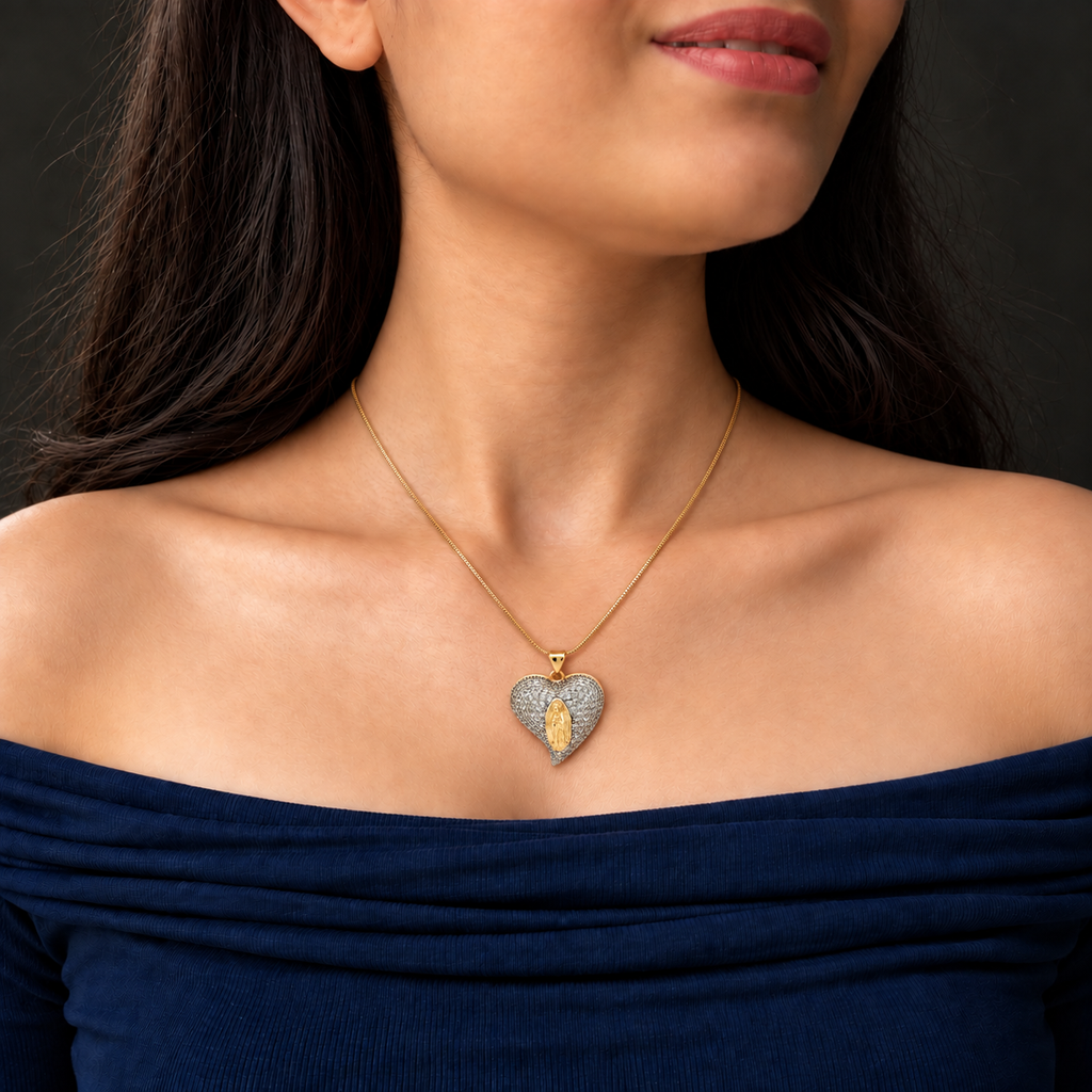 Gold-toned snake chain necklace with a heart-shaped pendant covered in clear sparkling stones and a raised golden religious figure at the centre.

Statement heart pendant necklace featuring silver-toned pavé detailing and gold accents, worn by a model.