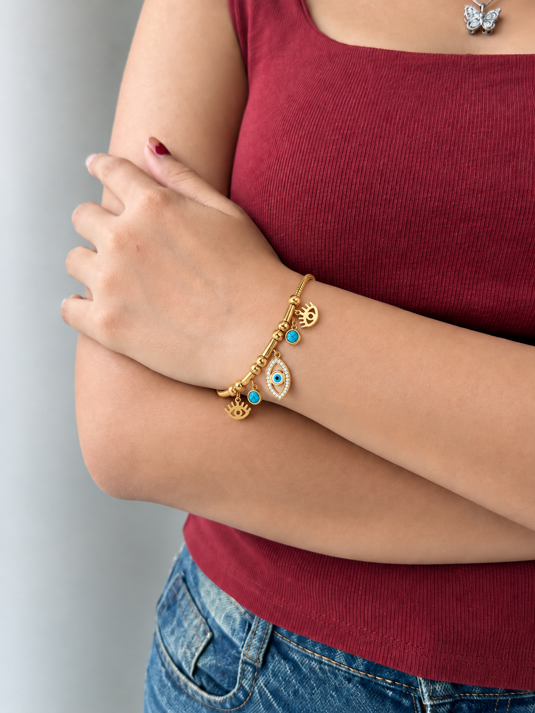 Gold-toned stainless steel charm bracelet featuring blue evil eye motifs, turquoise-coloured accents and an eye-shaped charm with sparkling white stones.
Decorative gold beads and a delicate chain with an adjustable extension, worn by a model.