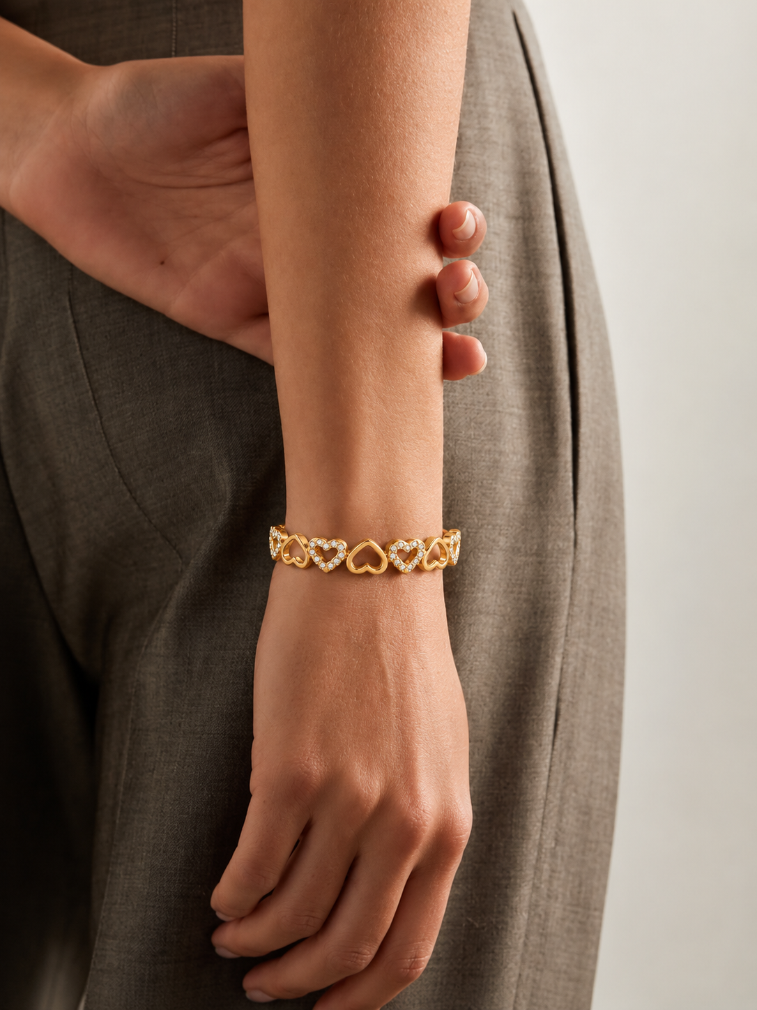 Gold-toned stainless steel bangle featuring alternating open-heart motifs with polished finishes and sparkling white stone accents with elegant hinged cuff design, worn by a model.