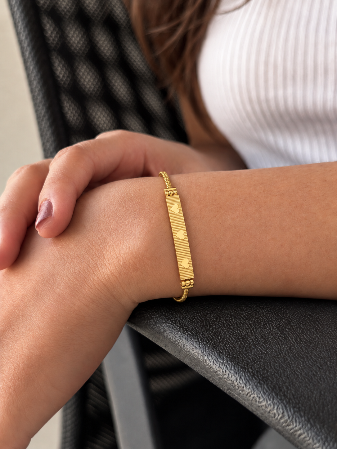 Gold-toned stainless steel bracelet featuring a textured rectangular bar with three engraved heart motifs.
Slim snake-chain bracelet with an adjustable extension, worn by a model.