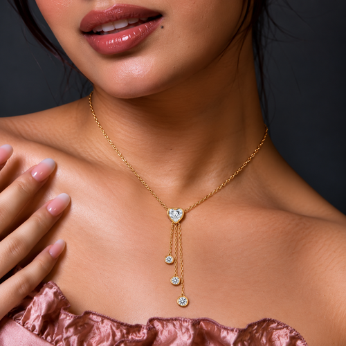Gold-toned lariat necklace with a heart-shaped clear centre stone and three cascading chains finished with round sparkling accents.

Close-up of a delicate gold heart pendant necklace featuring a graceful multi-chain drop design worn by a model.