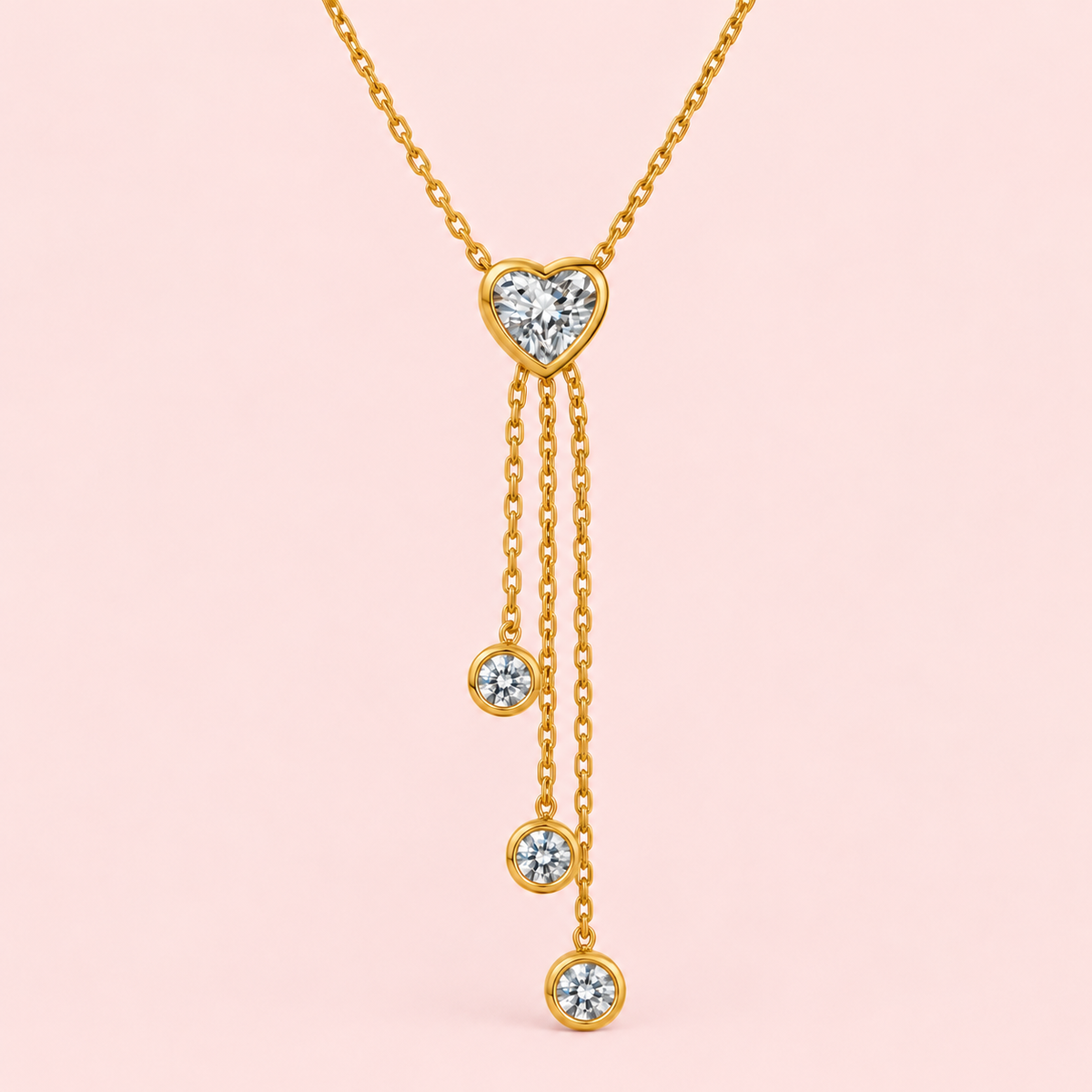 Gold-toned lariat necklace with a heart-shaped clear centre stone and three cascading chains finished with round sparkling accents.

Close-up of a delicate gold heart pendant necklace featuring a graceful multi-chain drop design on a pink background.