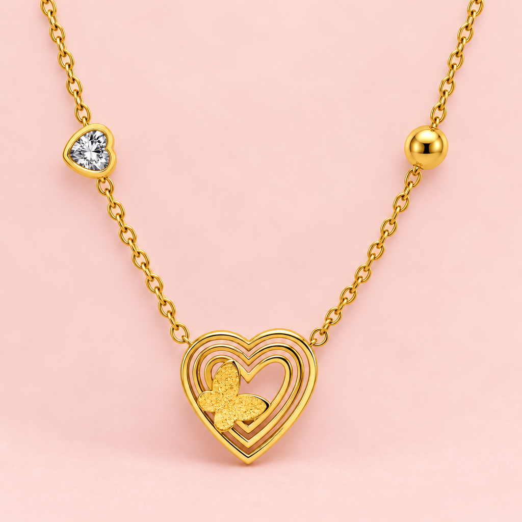 Gold-toned necklace featuring a layered open-heart pendant with a textured butterfly detail, a sparkling heart accent and polished heart-shaped elements along the chain.

Close-up of a delicate gold heart and butterfly necklace displayed against a clean pink background.