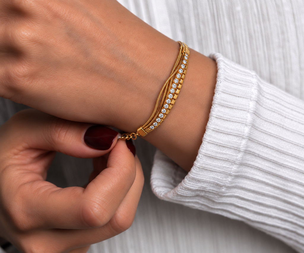 Gold-toned stainless steel multi-strand bracelet featuring clear sparkling stones and polished square accents.
Layered chain bracelet with an adjustable extension and lobster clasp, worn by a model