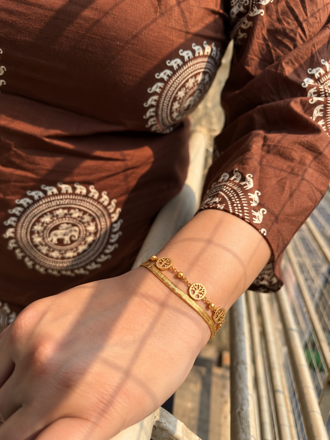 Gold-toned layered bracelet featuring three round openwork Tree of Life-inspired charms and small bead accents.
Designed with a sleek snake chain, delicate link chain and adjustable lobster clasp worn by a model.