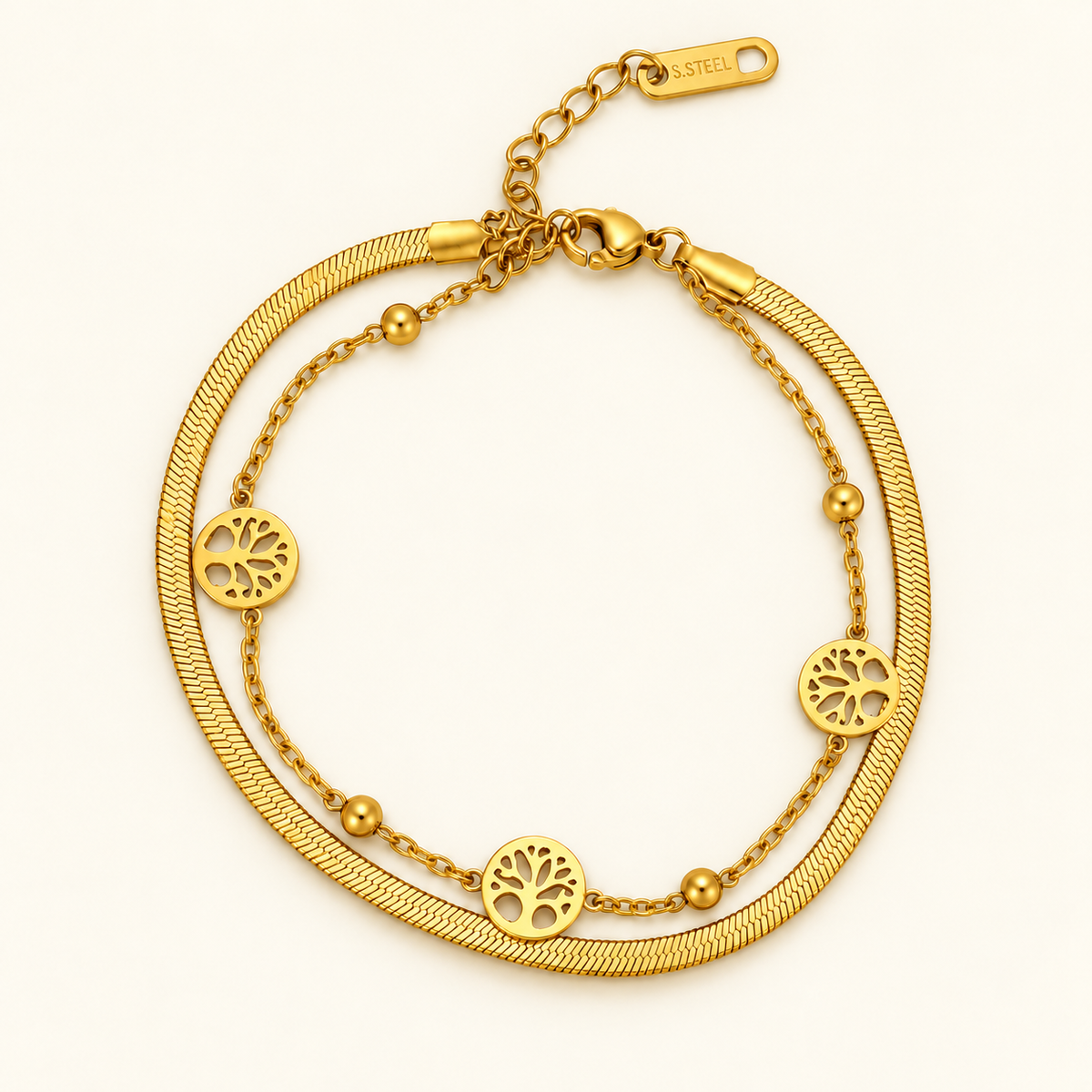 Gold-toned layered bracelet featuring three round openwork Tree of Life-inspired charms and small bead accents.
Designed with a sleek snake chain, delicate link chain and adjustable lobster clasp on a plain pink background.