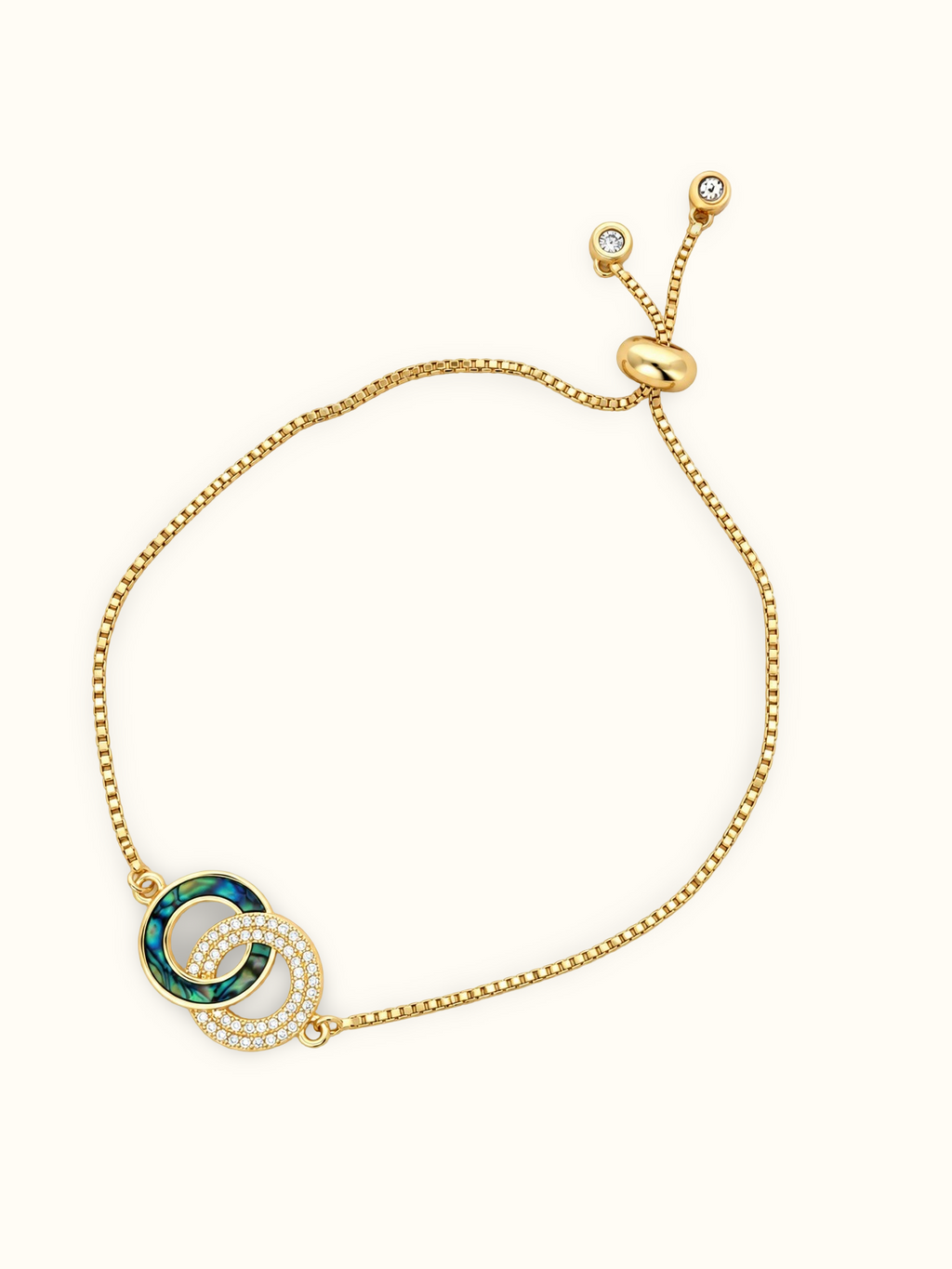 Gold-toned stainless steel bracelet featuring two intertwined circles, one with green enamel and the other set with sparkling white stones.
Delicate chain bracelet with an adjustable slider closure, displayed on a clean off-white background.