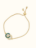 Gold-toned stainless steel bracelet featuring two intertwined circles, one with green enamel and the other set with sparkling white stones.
Delicate chain bracelet with an adjustable slider closure, displayed on a clean off-white background.
