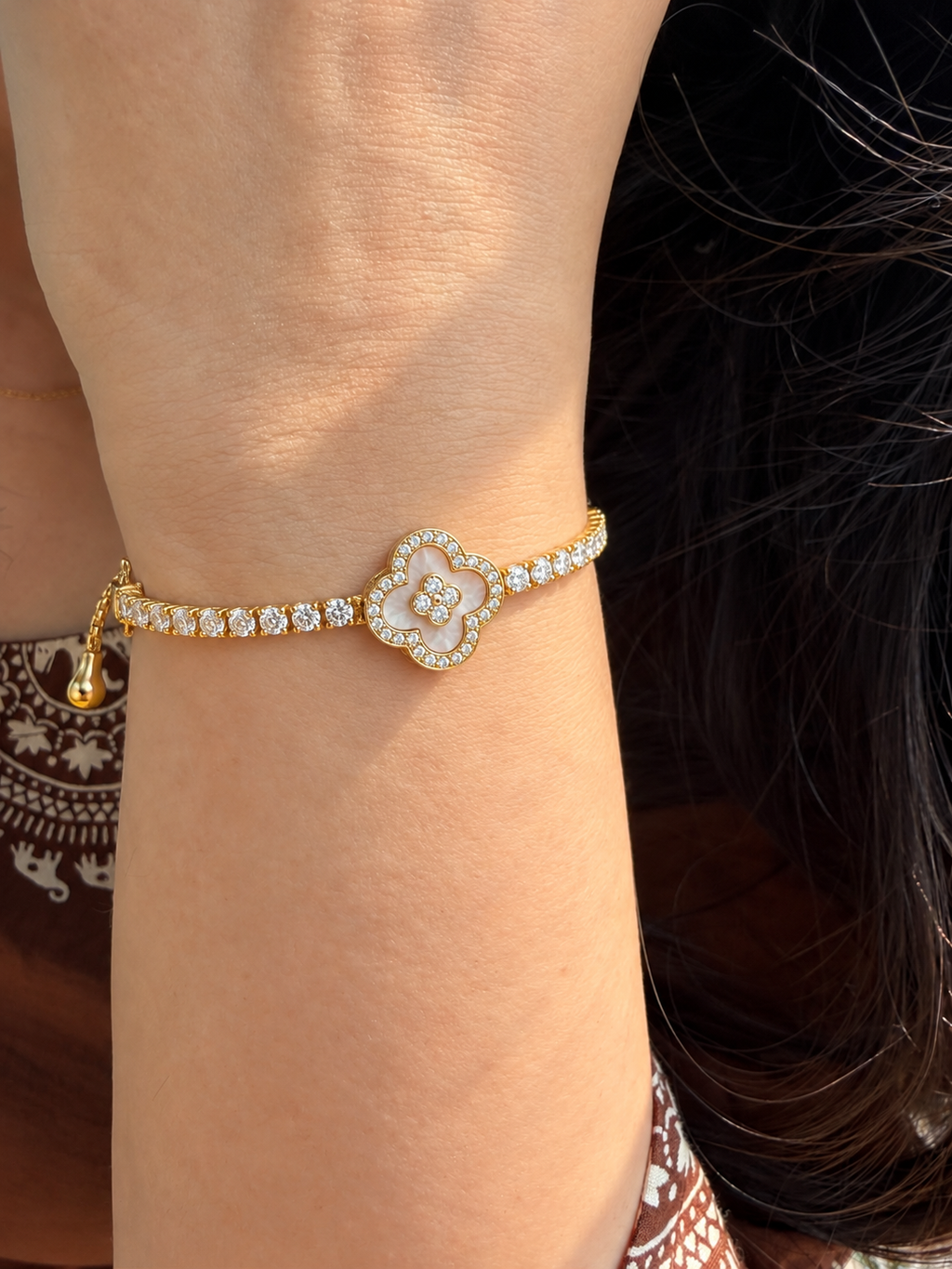 Gold-toned stainless steel slider bracelet featuring a four-leaf clover motif outlined with sparkling white stones and a floral centre.
Delicate gold chain with clear stone accents and an adjustable slider closure, worn by a model.