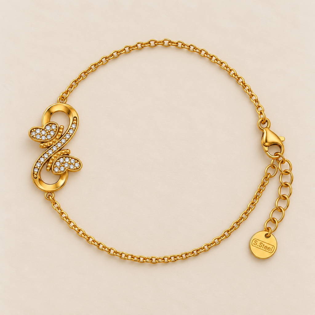 A delicate gold chain bracelet with a infinity design and two hearts facing each other filled with diamonds displayed against a light pink background.
