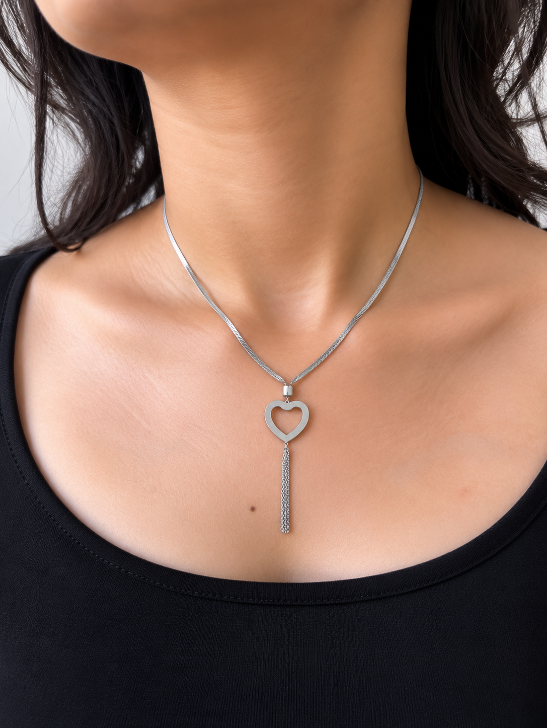 A silver thick chain necklace featuring a textured open heart pendant with a dangling chain, worn by a model.