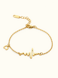 A delicate gold chain bracelet with a heartbeat line and heart charm, displayed against a light background.
