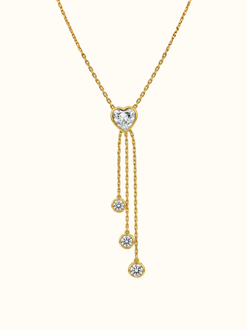 Gold-toned lariat necklace with a heart-shaped clear centre stone and three cascading chains finished with round sparkling accents.

Close-up of a delicate gold heart pendant necklace featuring a graceful multi-chain drop design on a white background.