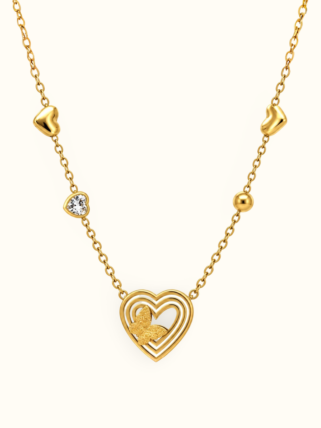 Gold-toned necklace featuring a layered open-heart pendant with a textured butterfly detail, a sparkling heart accent and polished heart-shaped elements along the chain.

Close-up of a delicate gold heart and butterfly necklace displayed against a clean white background.